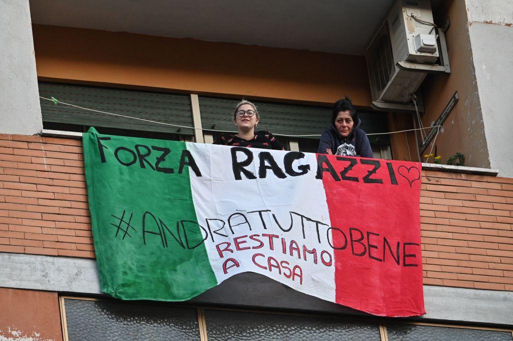 People sing, wave, and clap their hands next to a banner reading "Forza ragazzi hashtag #andratuttobene, restiamo a casa " (Come on, guys #everythingsgonnabeallright, we stay home) during a flash mob "Una canzone per l'Italia" (A song for Italy) at the Magliana district in Rome on March 15, 2020. (ANDREAS SOLARO/AFP via Getty Images)