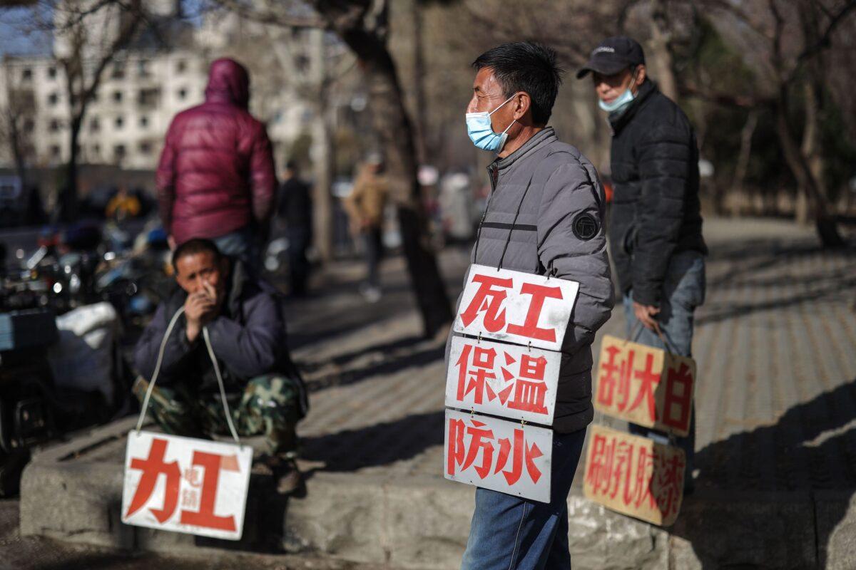 Day laborers hold signs advertising their skills as they wait to get hired for renovation works in Shenyang, China on March 27, 2020. (STR/AFP via Getty Images)