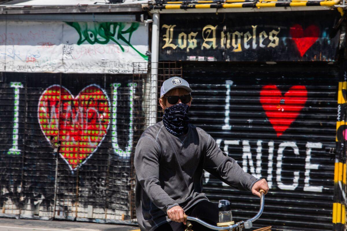 A man wearing a scarf as a face mask rides his bike in Venice Beach on April 4, 2020. (Apu Gomes/AFP via Getty Images)
