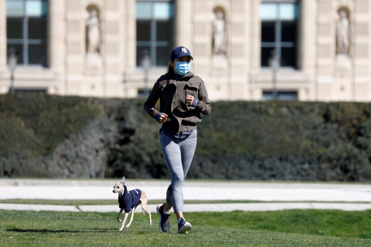 A lone jogger, wearing a protective mask, runs with her dog in the Tuileries Garden in Paris as a lockdown is imposed to slow the rate of COVID-19 spread in France on March 23, 2020. (Charles Platiau/File Photo/Reuters)