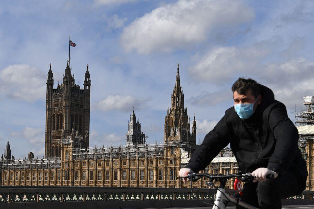 A man wearing a protective face mask cycles across Westminster Bridge, with the Houses of Parliament behind in central London on March 21, 2020. (Daniel Leal-Olivas/AFP via Getty Images)