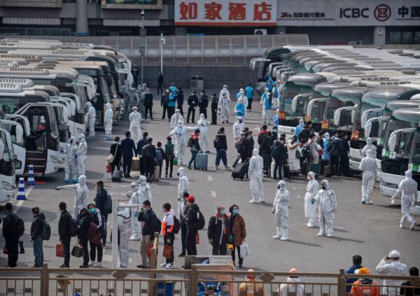 Chinese workers and health officials wear protective white suits as travelers from Wuhan gather to take buses as they are processed and taken to do 14 days of quarantine, after arriving on the first trains to Beijing on April 8, 2020. (Kevin Frayer/Getty Images)