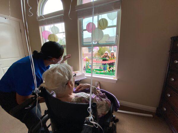 A caretaker helps Margaret Jones see her friend Lucy Cavazos through a window at The Kensington Redondo Beach for Jones’s 91st birthday on April 7, 2020. (Photo by Cristal Chavez/Courtesy of Lucy Cavazos)