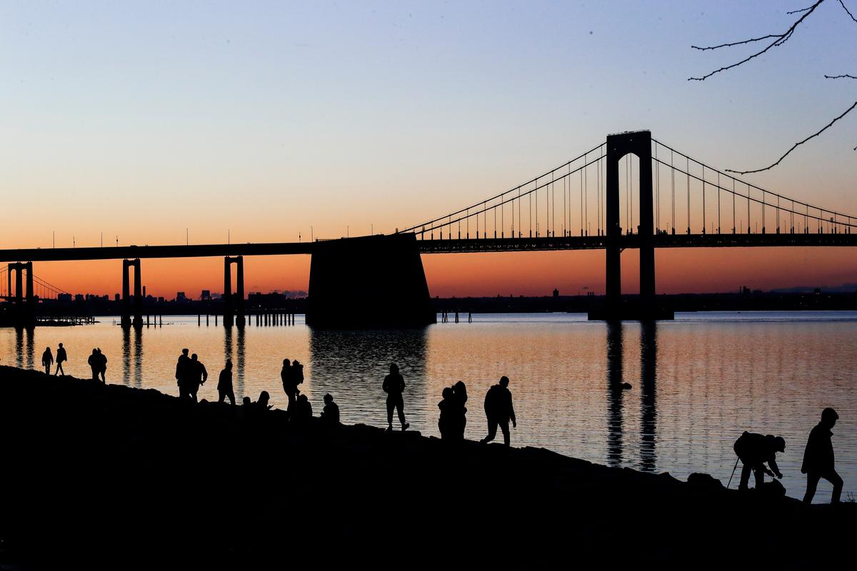 People gather to watch the sun set behind the Throgs Neck Bridge at Little Bay Park in the Queens borough of New York City on April 8, 2020. (Frank Franklin II/AP Photo)