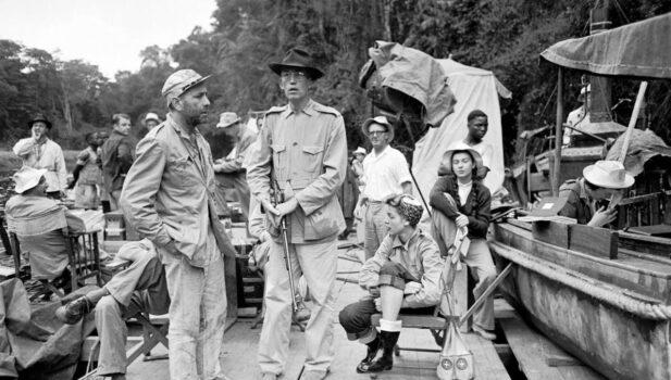 Humphrey Bogart (left of center) between takes with director John Huston (C) on the set of “The African Queen.” (United Artists)