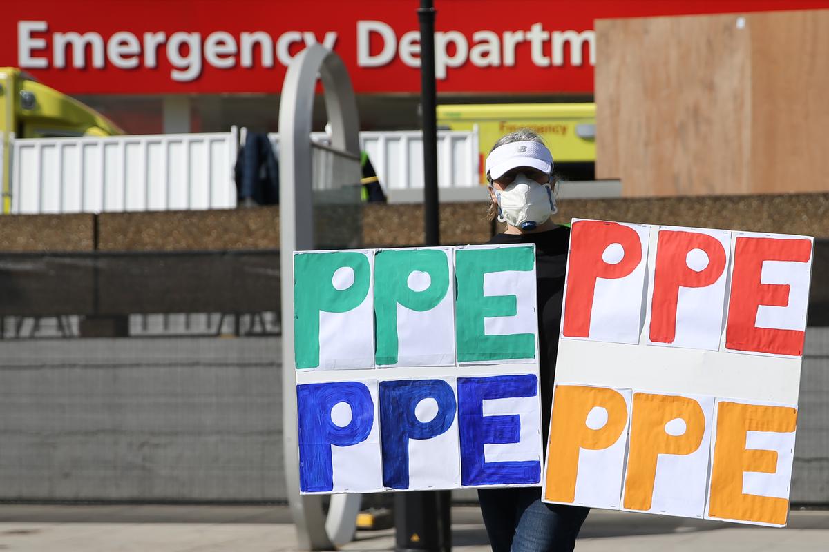 A demonstrator wearing a face mask protests holding signs reading "PPE" outside of St Thomas' Hospital in central London, England, on April 7, 2020 (©Getty Images | <a href="https://www.gettyimages.com/detail/news-photo/demonstrator-wearing-a-face-mask-holding-signs-reading-ppe-news-photo/1209331268?adppopup=true">ISABEL INFANTES</a>)