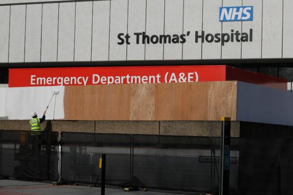 A worker paints a fence built over recent days to block the view of the ambulance entrance area outside St Thomas' Hospital in central London, where British Prime Minister Boris Johnson remains in intensive care as his CCP virus symptoms persist, on April 9, 2020. (Kirsty Wigglesworth/AP Photo)