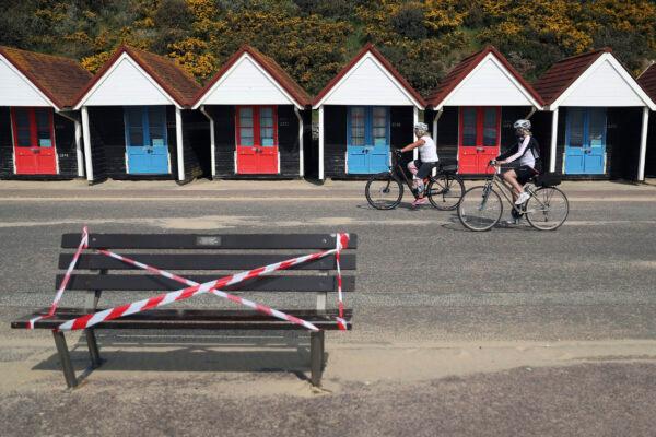 Cyclists make their way past a taped off bench on the sea front area at Bournemouth beach, as the UK continues in lockdown to help curb the spread of the CCP virus, in Bournemouth, England, on April 10, 2020. (Andrew Matthews/PA via AP)
