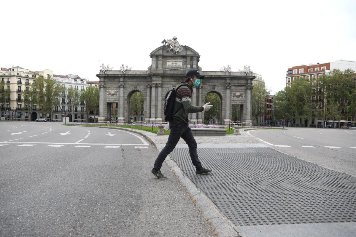 A man wearing a mask and gloves walks past the empty landmark Alcala Gate, amid the CCP virus outbreak in Madrid on April 9, 2020. (Sergio Perez/Reuters)
