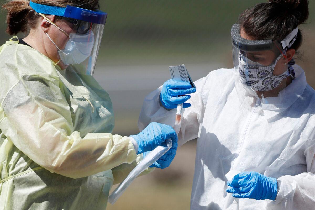In this March 31, 2020 file photo, medical technicians handle a vial containing a nasal swab at a drive-thru testing site in Wheat Ridge, Colorado. (David Zalubowski/AP Photo)