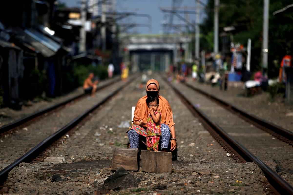 A woman and a child sit between rail tracks to enjoy sunshine as they believe it improves their immunity during social restrictions to prevent the spread of the CCP virus in Jakarta, Indonesia, on April 12, 2020. (Willy Kurniawan/Reuters)