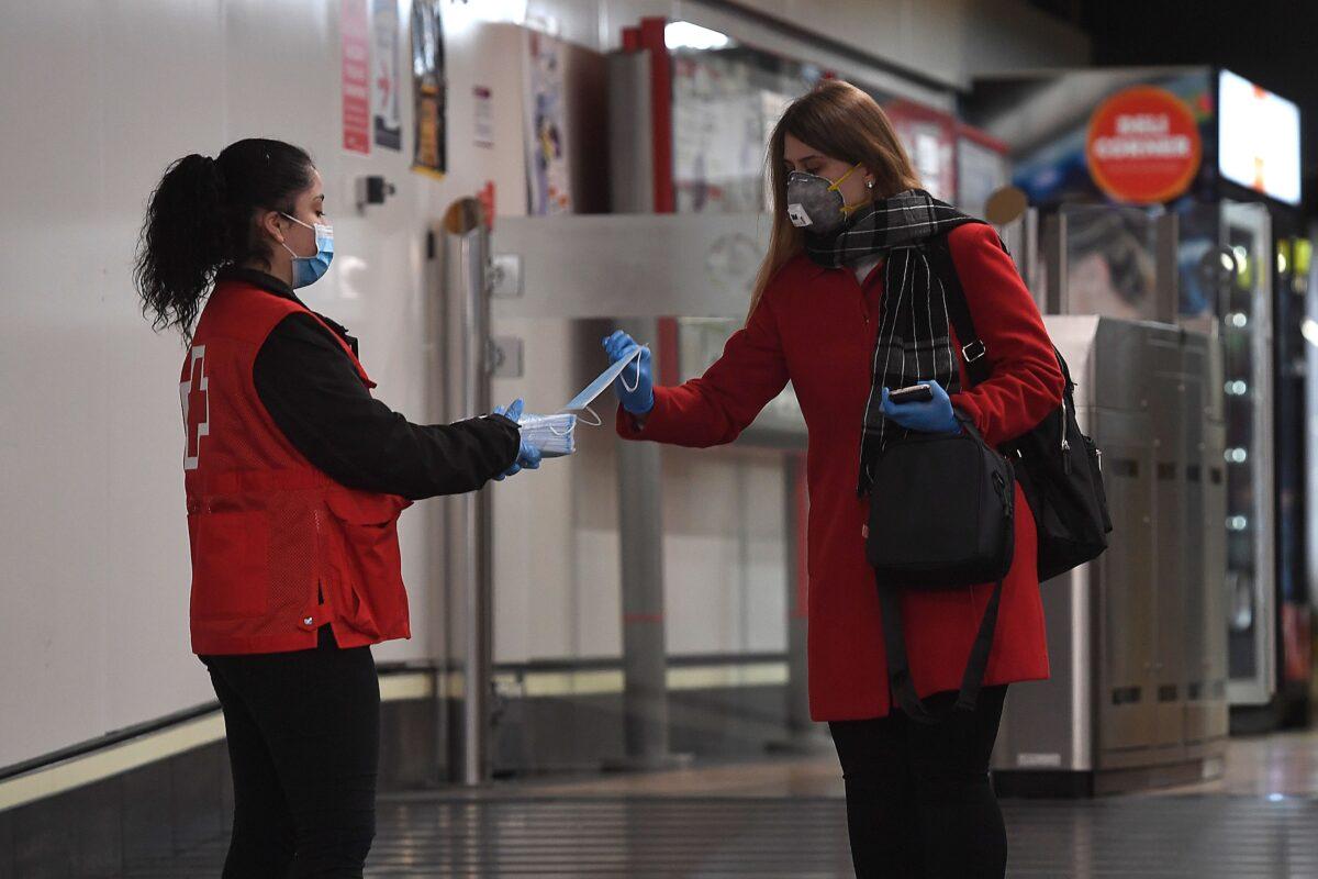 As some companies were set to resume operations at the end of a two-weeks halt of all non-essential activity amid a national lockdown to stop the spread of the COVID-19, a Spanish Red Cross volunteer distributes face masks at the Chamartin Station in Madrid on April 13, 2020. (Pierre-Philippe Marcou /AFP via Getty Images)