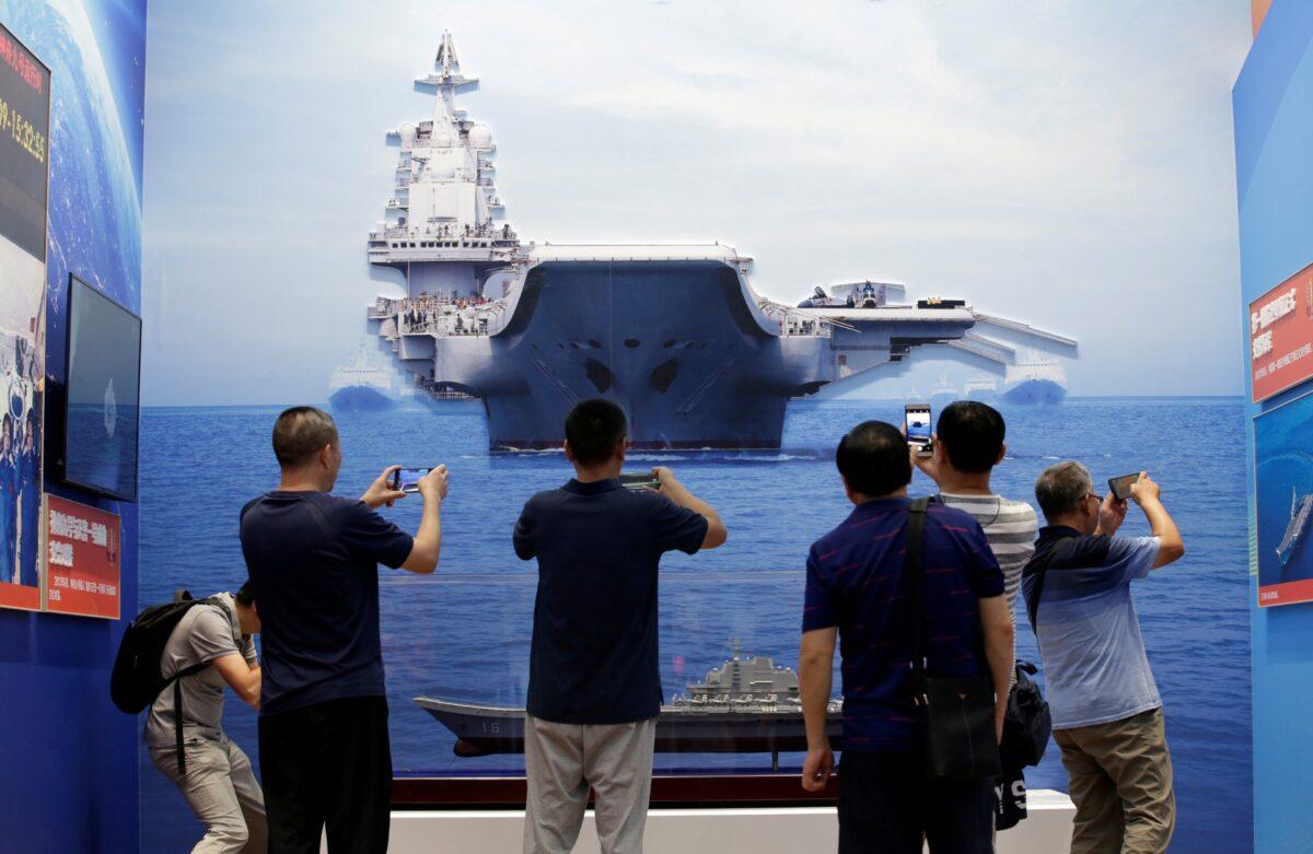 Visitors hold their mobile phones in front of exhibits showing People's Liberation Army (PLA) Navy's first aircraft carrier Liaoning, during an exhibition on China's achievements marking the 70th anniversary of the founding of the People's Republic of China (PRC) at the Beijing Exhibition Center, on Sept. 24, 2019. (Jason Lee/Reuters)