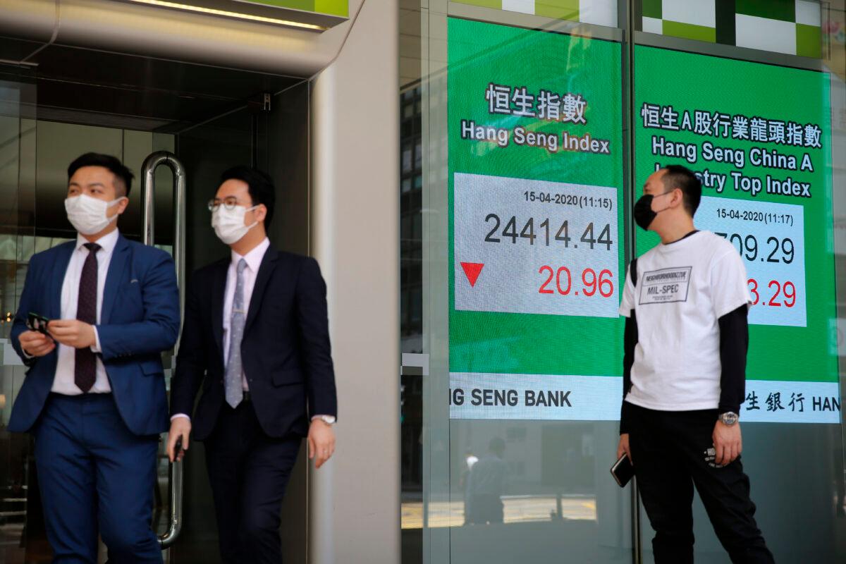 People wearing face masks walk past an electronic board showing Hong Kong share index outside a local bank in Hong Kong, on April 15, 2020. (Kin Cheung/AP Photo)