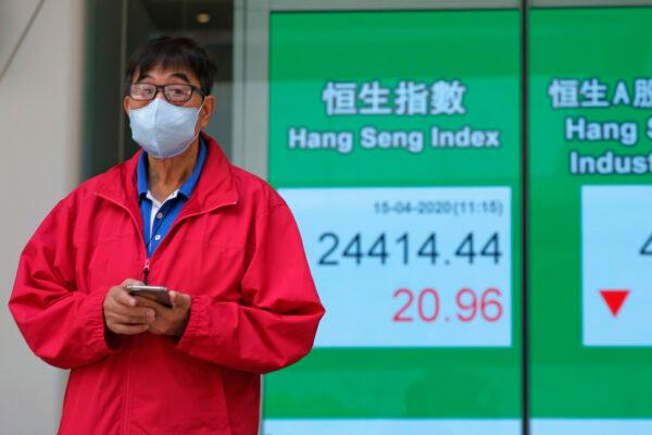 A masked man stands in front of an electronic board showing Hong Kong share index outside a local bank in Hong Kong, China, on April 15, 2020. (Kin Cheung/AP Photo)