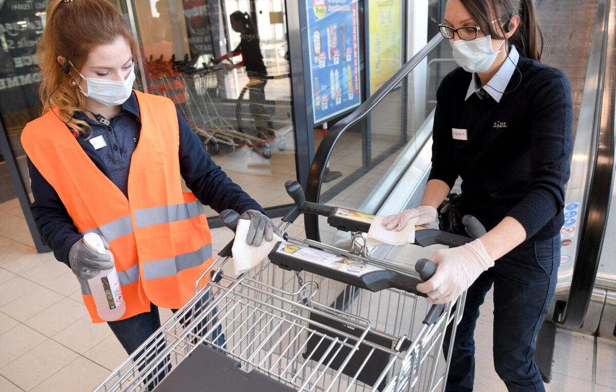 Employees of a supermarket wear face protection as they disinfect a shopping trolley in Vienna on April 6, 2020. (Roland Schlager/APA/AFP/Getty Images)
