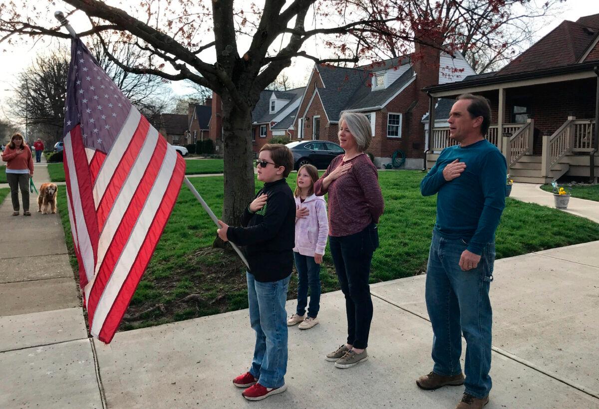 Zach Stamper holds the U.S. flag while his sister Juliette and parents Jennifer and Tim recite the Pledge of Allegiance in the driveway of their home in Kettering, Ohio, on April 7, 2020, as next door neighbor, Ann Painter, left, participates. The Pledge has become a morning ritual in their neighborhood since schools closed due to the COVID-19 threat. (Mitch Stacy/AP Photo)