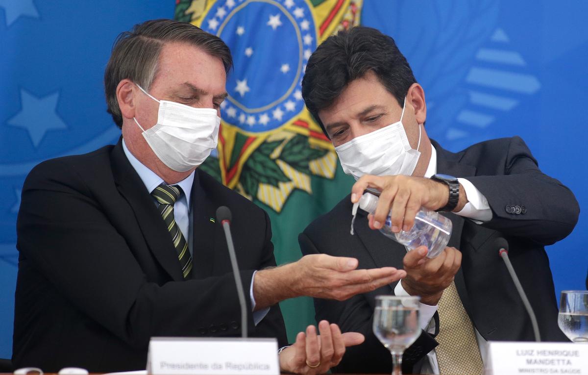 Brazilian Health Minister Luiz Henrique Mandetta (R) gives hand sanitizer to President Jair Bolsonaro, both using protective masks, during a press conference about government plans and measures about the CCP virus crisis in Brazil, at the Planalto Palace in Brasilia, Brazil, on March 18, 2020. (Andre Coelho/Getty Images)