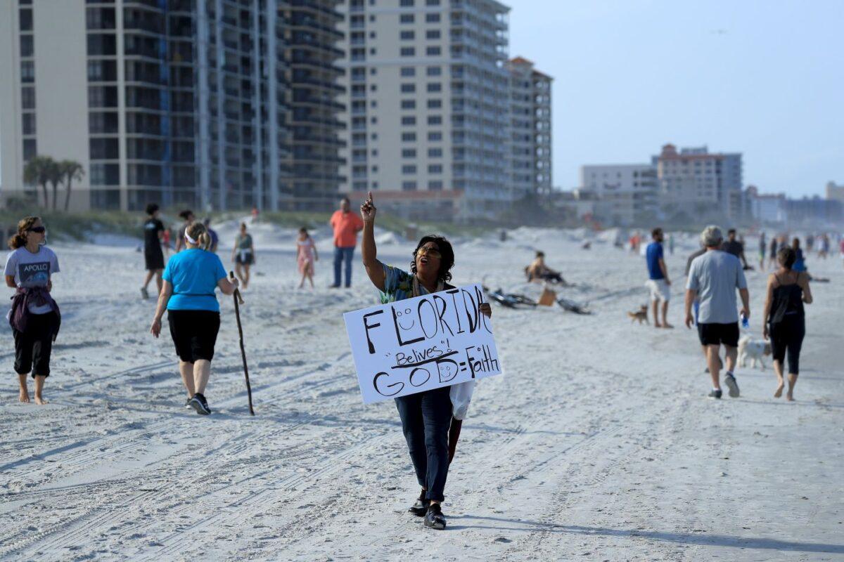 A person carries a sign at the beach after Florida Gov. Ron DeSantis reopened state beaches with some restrictions, in Jacksonville Beach, Fla., on April 17, 2020. (Sam Greenwood/Getty Images)