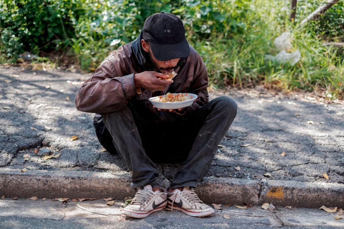 A homeless man eats his food using a credit card during a food distribution by the Cleveland Civic Committee in Cleveland, near Johannebsurg, South Africa, on April 20, 2020. (Luca Sola /AFP via Getty Images)