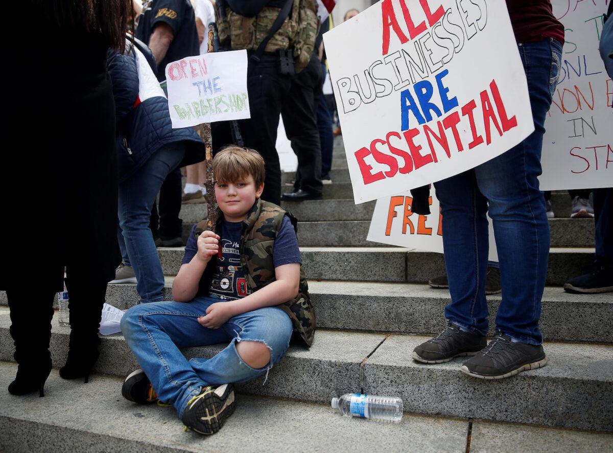 A boy holds a sign reading "Open the barbershop" as hundreds gather to protest against the state's extended stay-at-home order on the steps of the Capitol building in Olympia, Wash., on April 19, 2020. (Lindsey Wasson/Reuters)