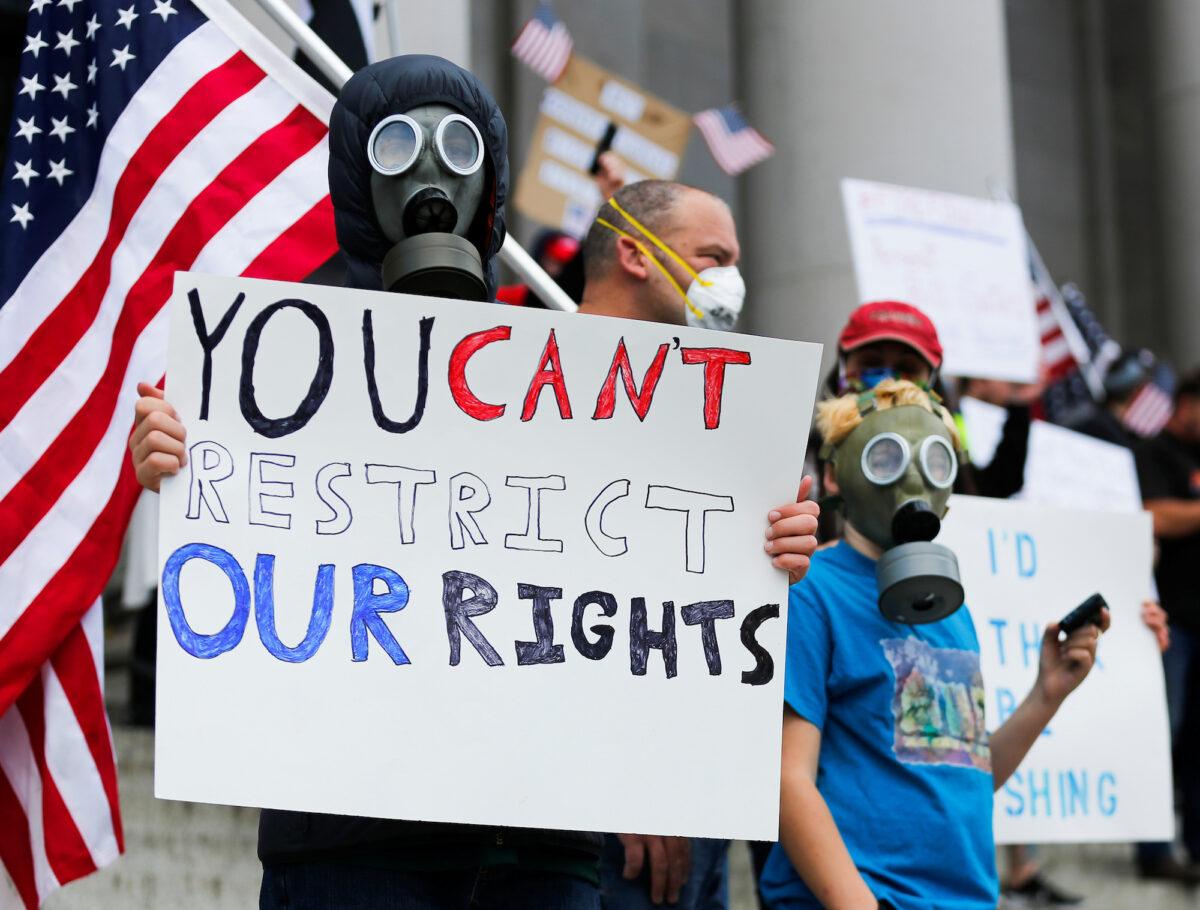 A person wearing a gas mask holds a sign as hundreds gather to protest against the state's extended stay-at-home order to help slow the spread of the CCP virus, which causes COVID-19, at the Capitol building in Olympia, Washington, on April 19, 2020. (Reuters/Lindsey Wasson)