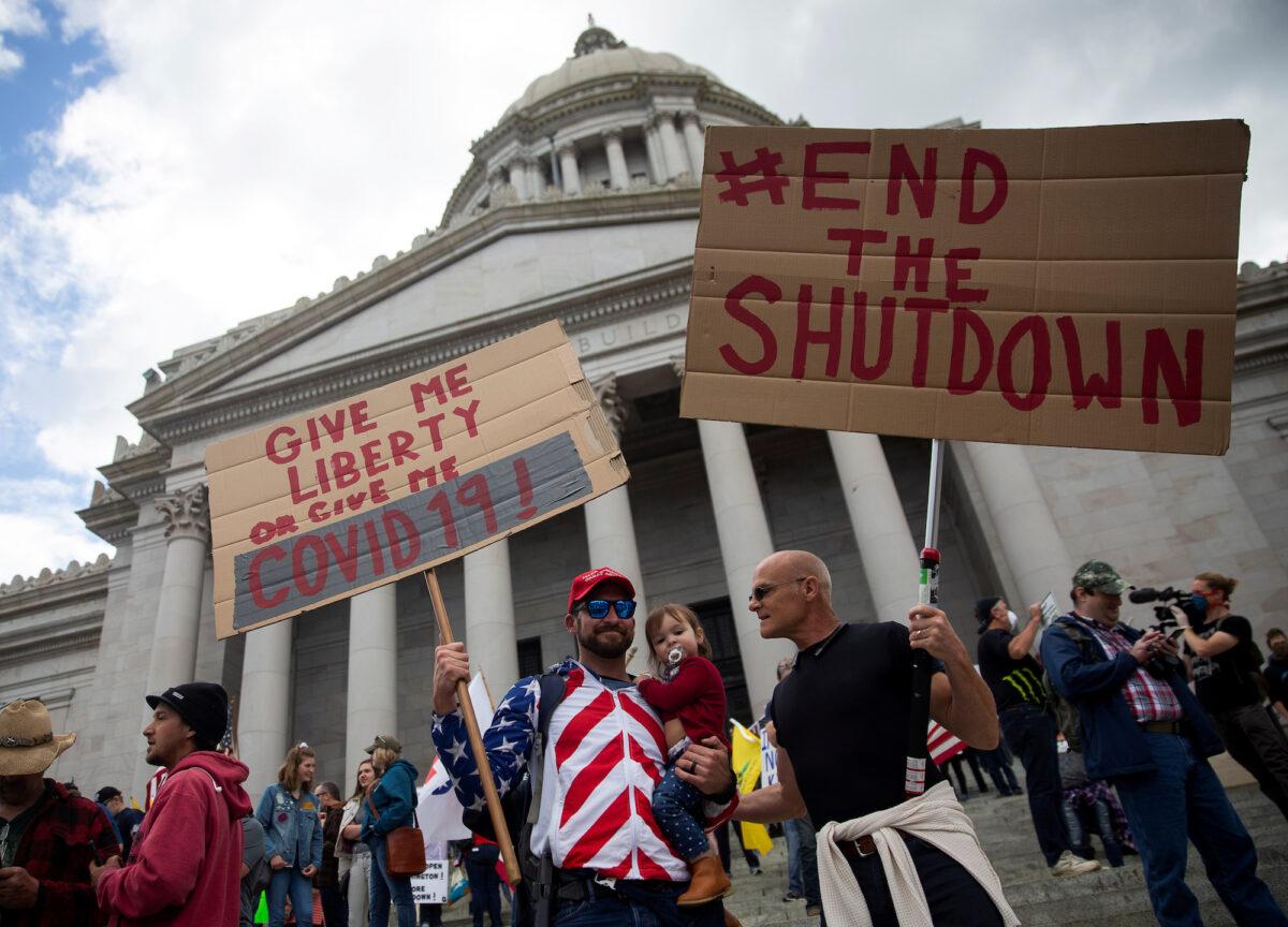 Two men hold signs as they protest against the state's extended stay-at-home order as hundreds gather to demonstrate at the Capitol building in Olympia, Wash., on April 19, 2020. (Reuters/Lindsey Wasson)