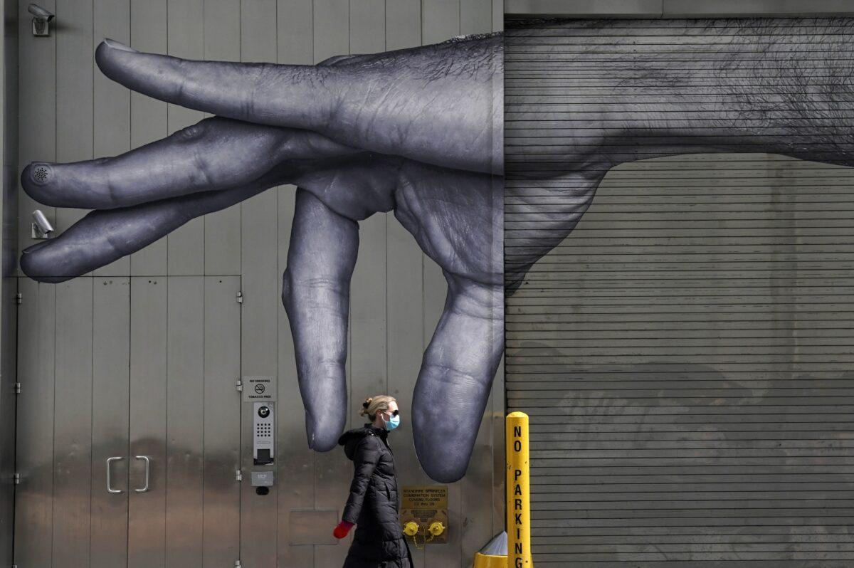 A woman in a mask walks past a mural of a hand on the side of a building in Manhattan, New York City on April 22, 2020. (Timothy A. Clary/AFP via Getty Images)