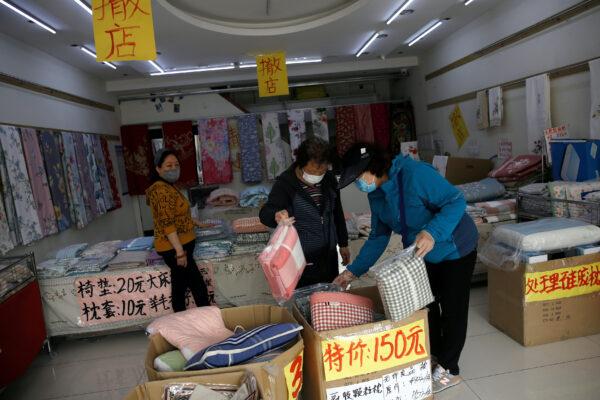 Customers wearing face masks shop bed linen under business closure notices inside a home linen store whose business has been struggling since the COVID-19 outbreak, in Beijing, China, on April 14, 2020. (Tingshu Wang/Reuters)