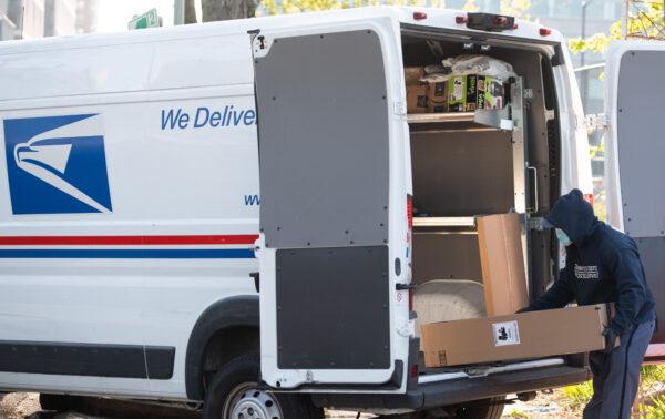 A mailman wearing a mask and gloves to protect himself and others from COVID-19, loads a postal truck with packages at a United States Postal Service (USPS) post office location in Washington, on April 16, 2020. (Saul Loeb/AFP via Getty Images)