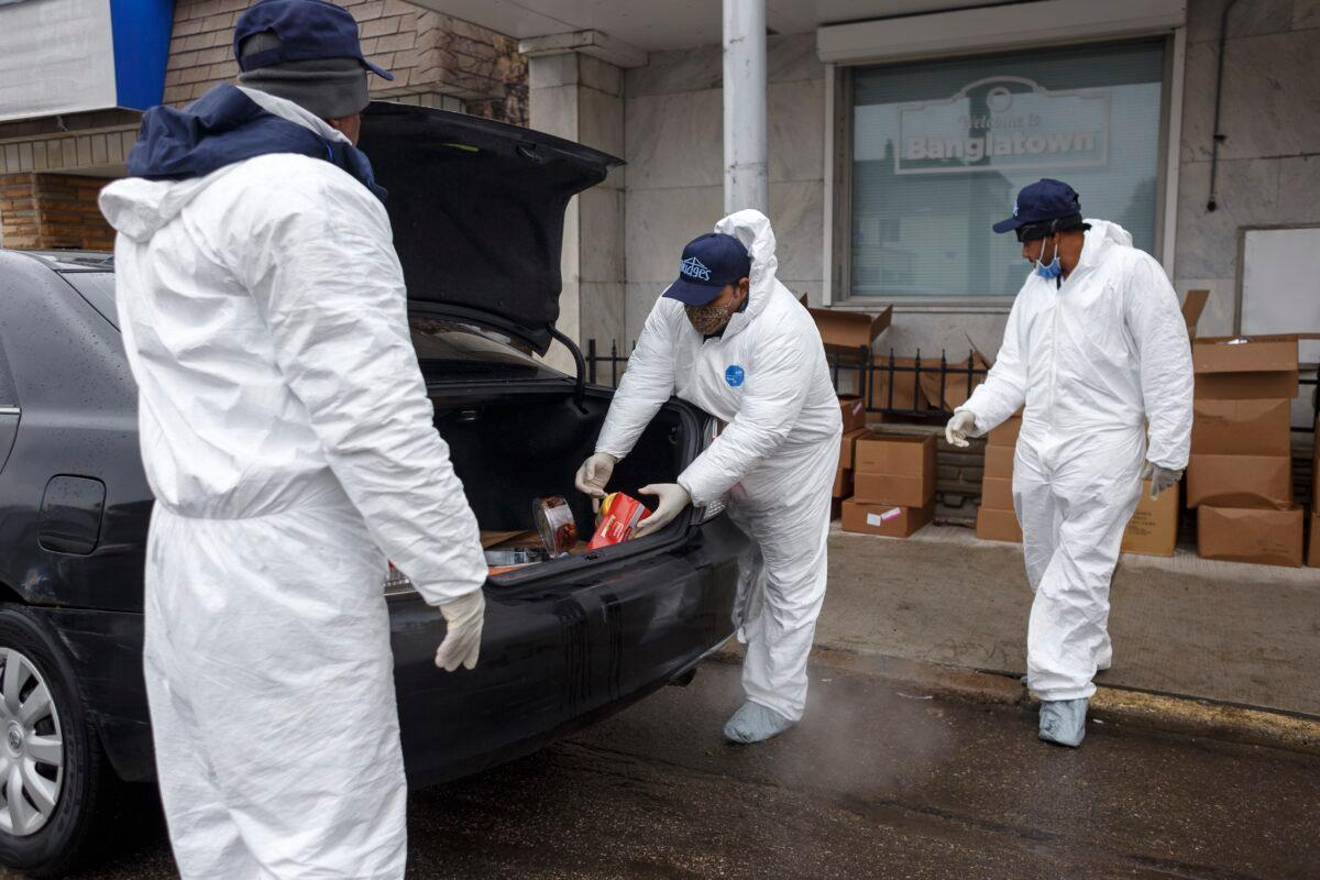 Armani Asad, owner of Maa Fashion, center, places donated food in the trunk of a car while Nazel Huda, left, holds open the trunk door on the first day of Ramadan in Hamtramck, Michigan on April 23, 2020. (Elaine Cromie/Getty Images)