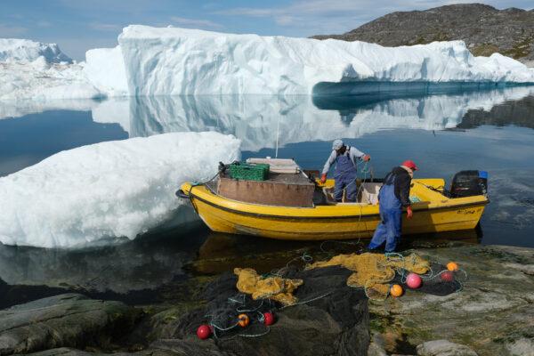 Inuit fishermen prepare a net as free-floating ice floats behind at the mouth of the Ilulissat Icefjord during unseasonably warm weather near Ilulissat, Greenland on July 30, 2019. (Sean Gallup/Getty Images)
