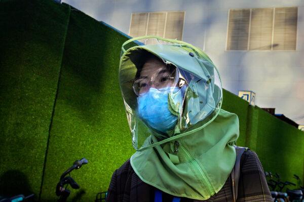 A woman—wearing a facemask and a design clothing face shield amid the concerns over the CCP virus—walks on a street in Beijing, China on April 20, 2020. (Nicolas Asfouri/AFP via Getty Images)