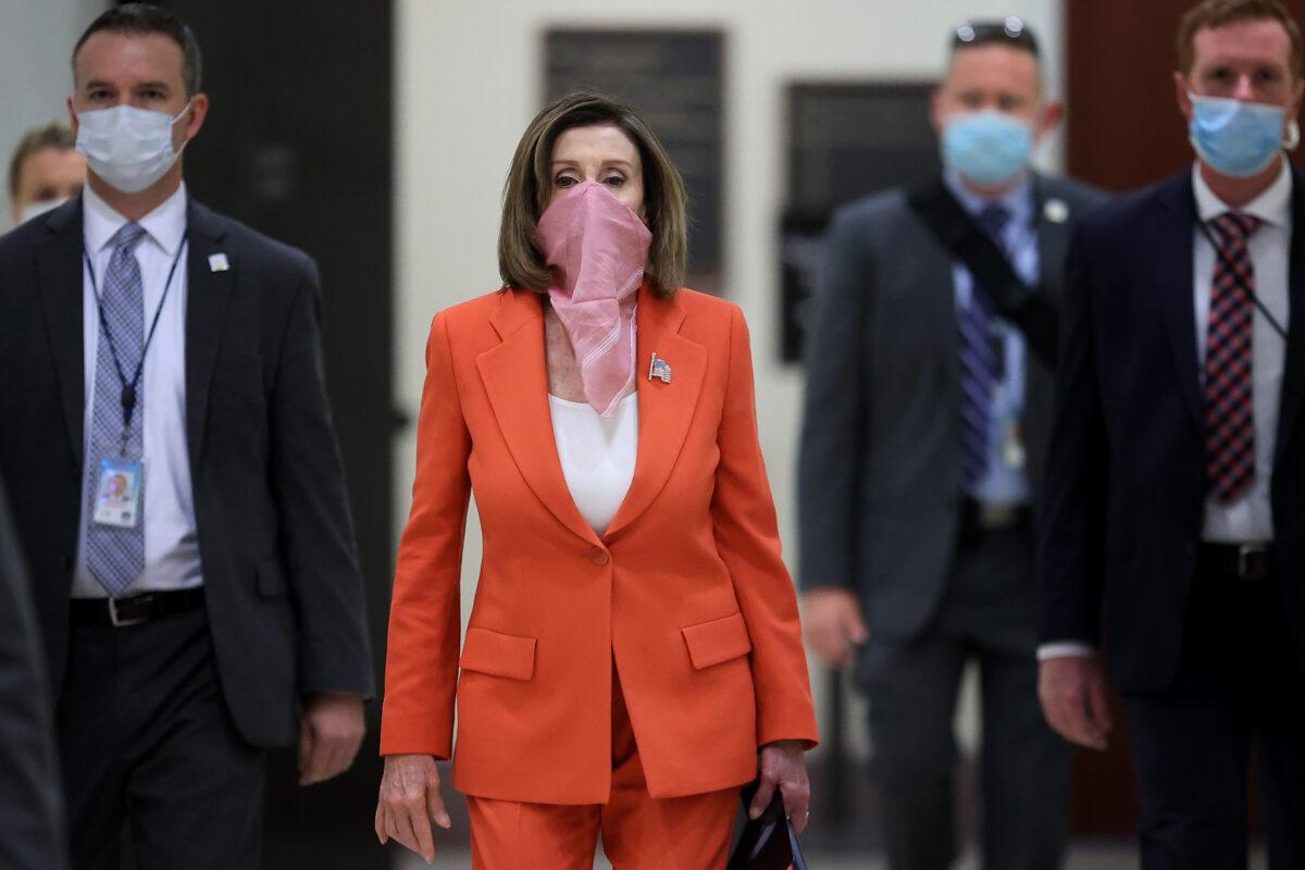 Wearing a scarf over her mouth and nose, House Speaker Nancy Pelosi (D-Calif.) is surrounded by security and staff as she arrives for her weekly news conference during the COVID-19 pandemic at the U.S. Capitol in Washington, on April 24, 2020. (Chip Somodevilla/Getty Images)