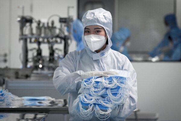 A worker wearing a protective suit holds masks to package at Naton Medical Group, a company which makes medical equipment in Beijing, on April 24, 2020. (Wang Zhao/AFP via Getty Images)
