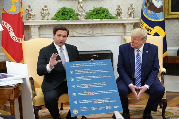 President Donald Trump listens as Florida Gov. Ron DeSantis holds up a sign during a meeting in the Oval Office of the White House in Washington on April 28, 2020. (Mandel Ngan/AFP via Getty Images)