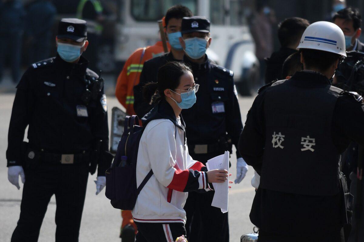 A student walks past police and officials as she arrives at a high school in Beijing on April 27, 2020. (Greg Baker/AFP via Getty Images)