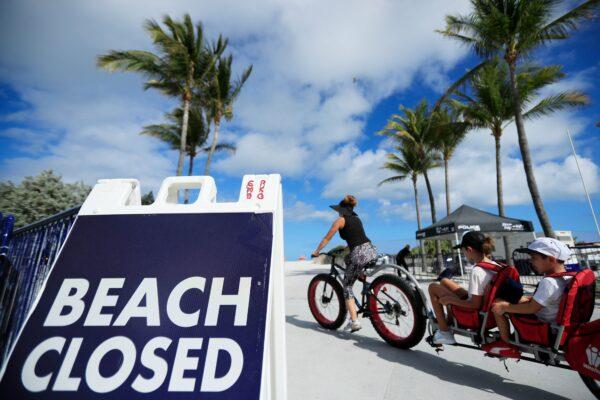 A cyclist with a trailer for children passes a "Beach Closed" sign on the boardwalk in Miami Beach, Fla., on March 22, 2020. (Cliff Hawkins/Getty Images)