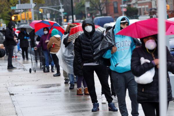 People wearing protective face masks wait in line to receive free food at a curbside pantry for needy residents in New York City, on April 24, 2020. (Reuters/Mike Segar)