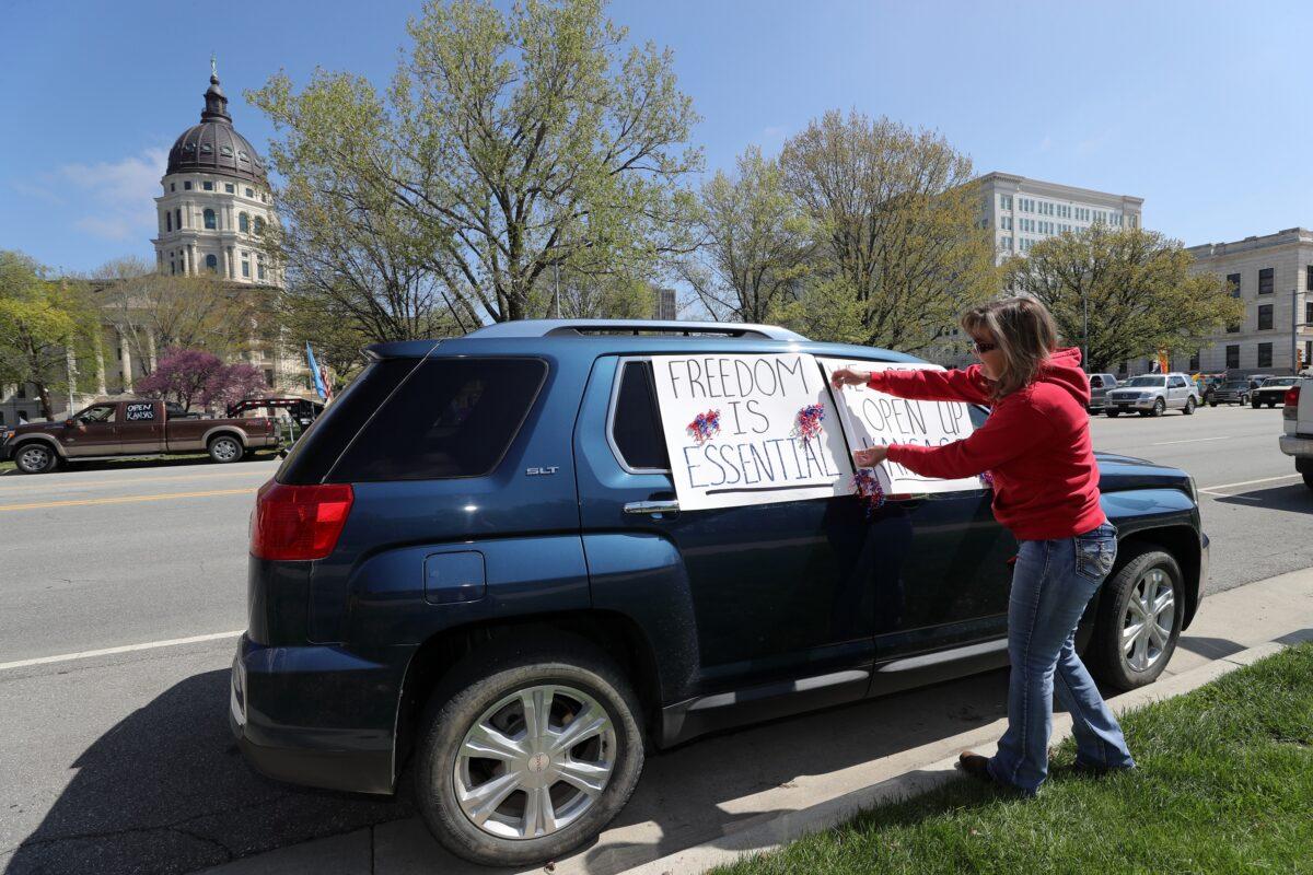 A woman tapes a sign to her car in front of the state capitol building as protesters demand that businesses be allowed to open up, people allowed to work, and lives returned to normal in Topeka, Kansas, on April 23, 2020. (Jamie Squire/Getty Images)