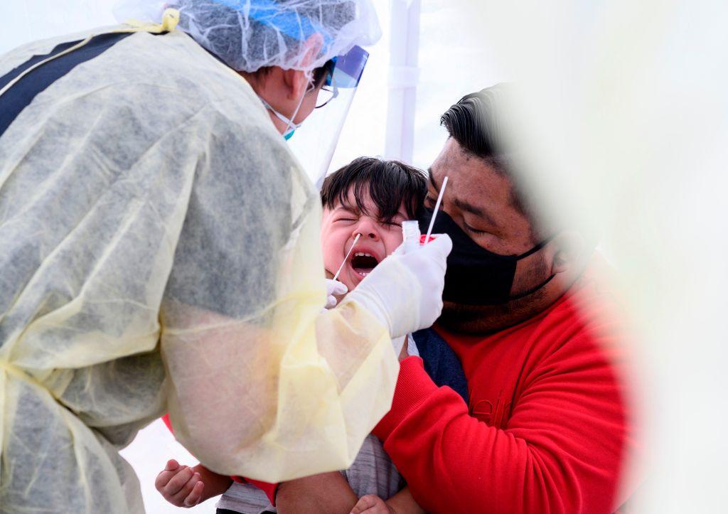 Jose Vatres (R) holds his son Aidin, who reacts as a nurse practitioner Alexander Panis (L) takes a nasal swab sample to test for COVID-19 at a mobile testing station in a public school parking area in Compton, Calif., on April 28, 2020. (Robyn Beck/AFP/Getty Images)