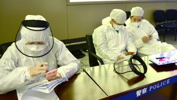 Workers in protective suits are seen at a registration point for passengers at an airport in Harbin, capital of Heilongjiang province bordering Russia, following the spread of the CCP virus in the country, China, on April 11, 2020. (Huizhong Wu/Reuters)