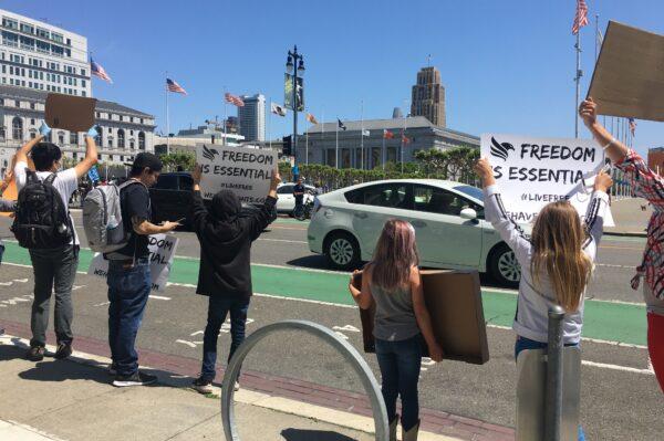 San Francisco protesters show signs as cars pass by City Hall on May 1, 2020. (Ilene Eng/The Epoch Times)