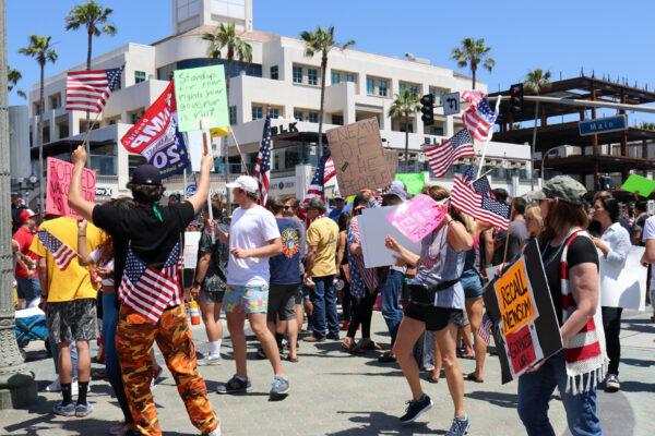 Protesters wave flags and carry signs in Huntington Beach, Calif., on May 1, 2020. (Jamie Joseph/The Epoch Times)