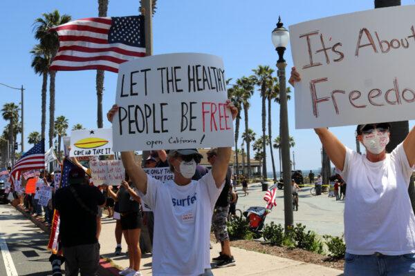 Protesters hold signs at a gathering in Huntington Beach, Calif., on May 1, 2020. (Jamie Joseph/The Epoch Times)