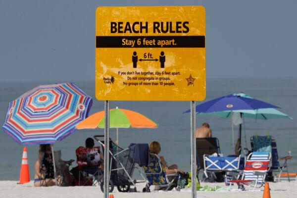 Beachgoers sunbathe near a beach rules sign after Clearwater Beach officially reopened to the public in Clearwater Beach, Fla., on May 4, 2020. (Chris O'Meara/AP Photo)