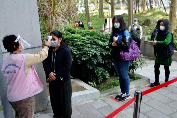 A masked local resident (2nd L) has her temperature checked as people line up to buy face masks from vending machines at the Xinyi District Health Center in Taipei, Taiwan, on April 14, 2020. (Sam Yeh /AFP/Getty Images)