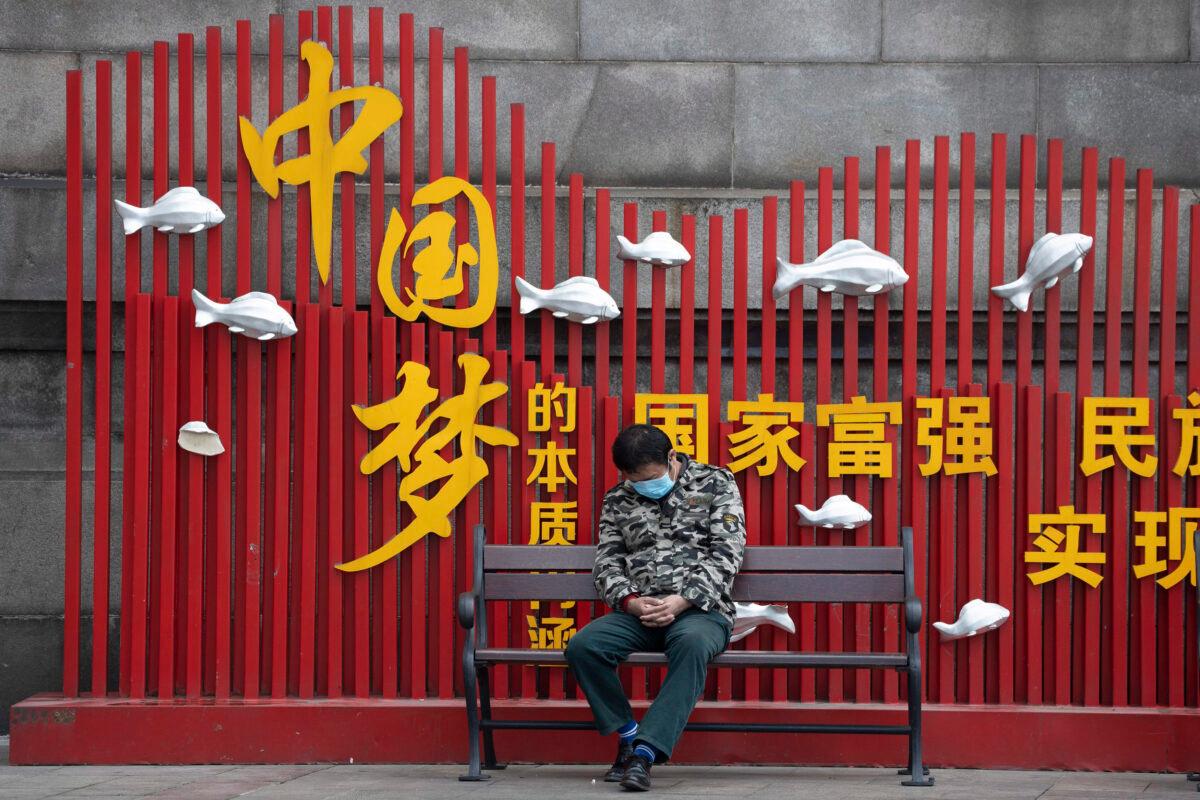 A resident wearing mask naps on a bench near Beijing's propaganda slogan "Chinese dream" in Wuhan, China, on April 1, 2020. (Ng Han Guan/AP Photo)