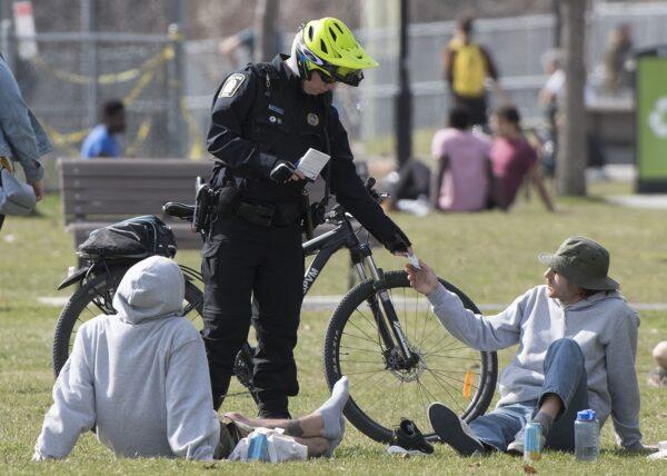 A police officer checks the identification of a man in a park in Montreal on May 2, 2020, as police patrol the park to make sure people are observing physical distancing protocols amid the pandemic. (Graham Hughes/The Canadian Press)