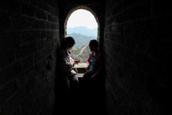 Two children wearing face masks rest during their visit to the Great Wall of China in Beijing on April 18, 2020. (Wang Zhao/AFP via Getty Images)